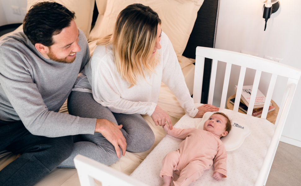 Parents regardent bébé dans un berceau à côté du lit avec oreiller nouveau-né plagiocéphalie blanc