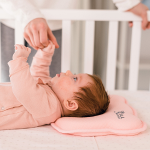 Bébé fille couchée dans le berceau avec oreiller de plagiocéphalie rose tient sa main à sa mère