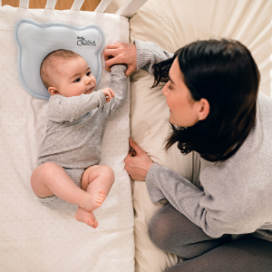 Maman sur lit regarde bébé dans un berceau à côté du lit avec oreiller bébé plagiocéphalie bleu