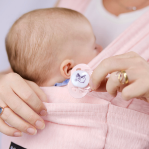 Bébé nouveau-né en écharpe Koala Babycare rose avec les mains de maman et sucette 